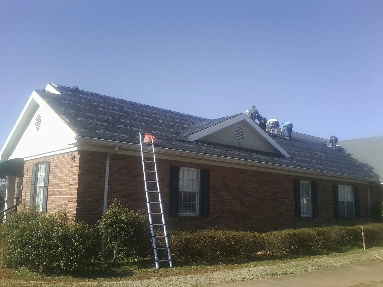 Crew tearing shingles off a brick ranch roof with a ladder set — Emergency Roof Repair work by our crew in Littleton