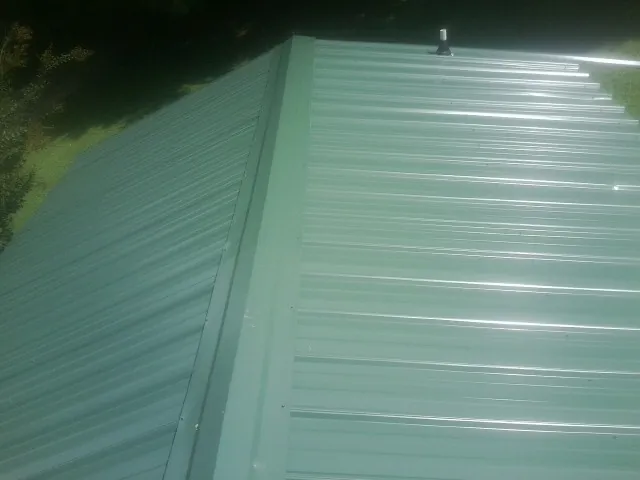 New green metal panels meeting at the ridge of a roof — Flat Roof Repair work by our crew in Littleton