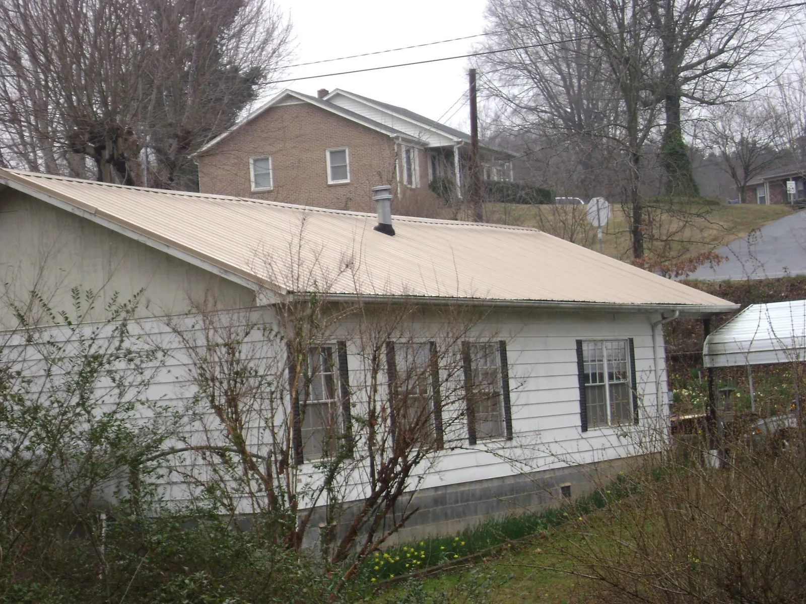 Tan metal roof on a white sided house set into a hillside — Commercial Roofing by Roofing Brothers in Littleton